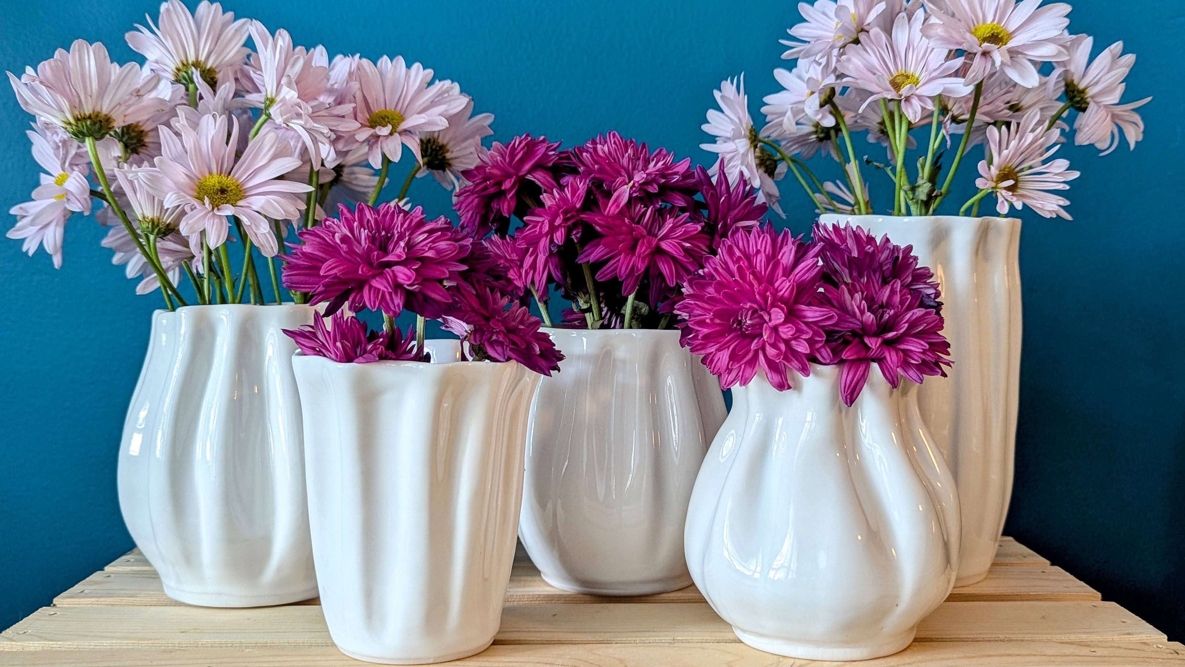 White vases with pink and purple flowers against a blue background